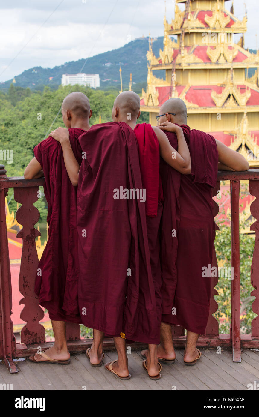 Three young monks looking at the Mandalay Royal Palace complex from the Nanmyintsaung watchtower, Myanmar (Burma). Stock Photo