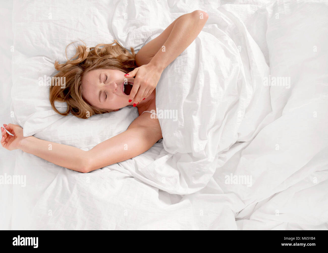 Tired sleepy woman waking up and yawning with a stretch after sleep in bed Stock Photo