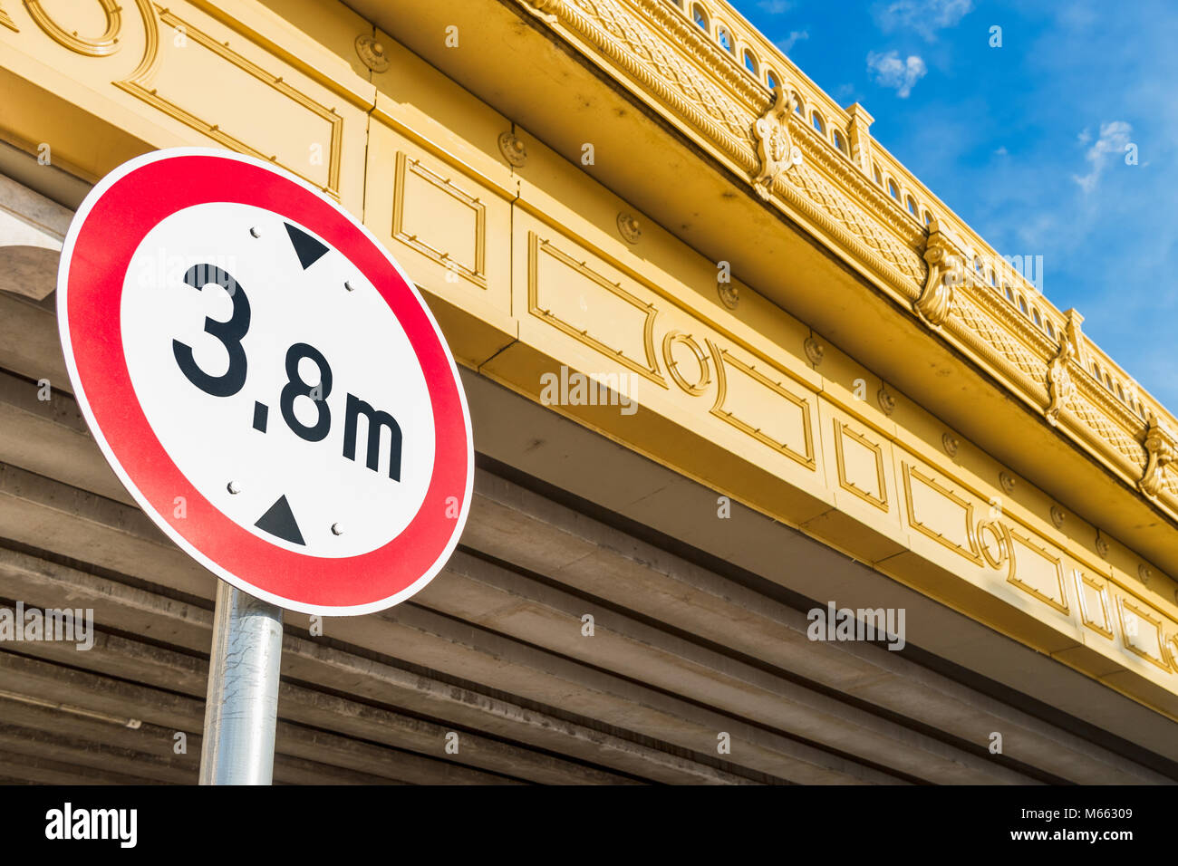 Circular low bridge regulatory road sign with red ring showing the height limit on non-arch yellow bridge against blue sky Stock Photo