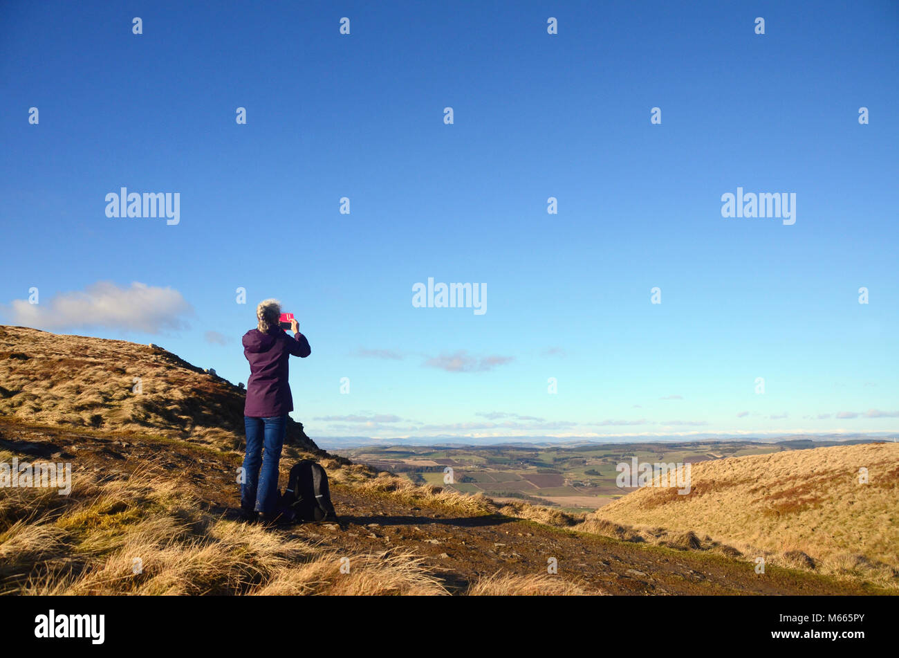 A woman takes a photo from the Lomond hills in Fife, of the snowy peaks of the cairngorms seen in the distance. Stock Photo