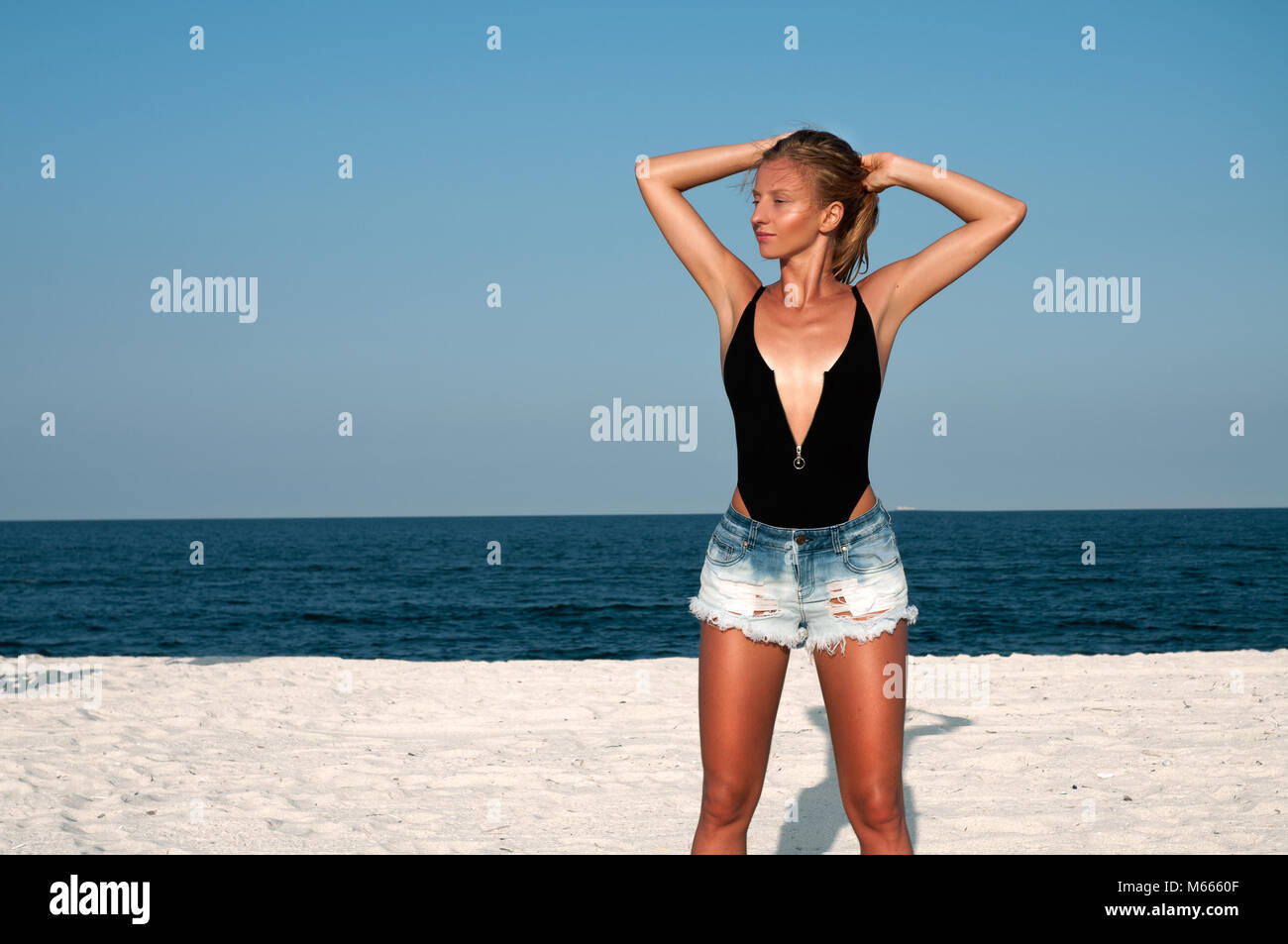 Beautiful woman in black swimsuit and jeans shorts on the beach. Summer