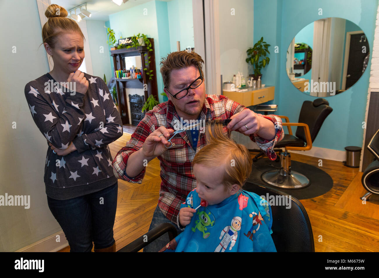Caucasian Toddler Boy Has His Hair Cut By A Barber As His Mom Watches Stock Photo