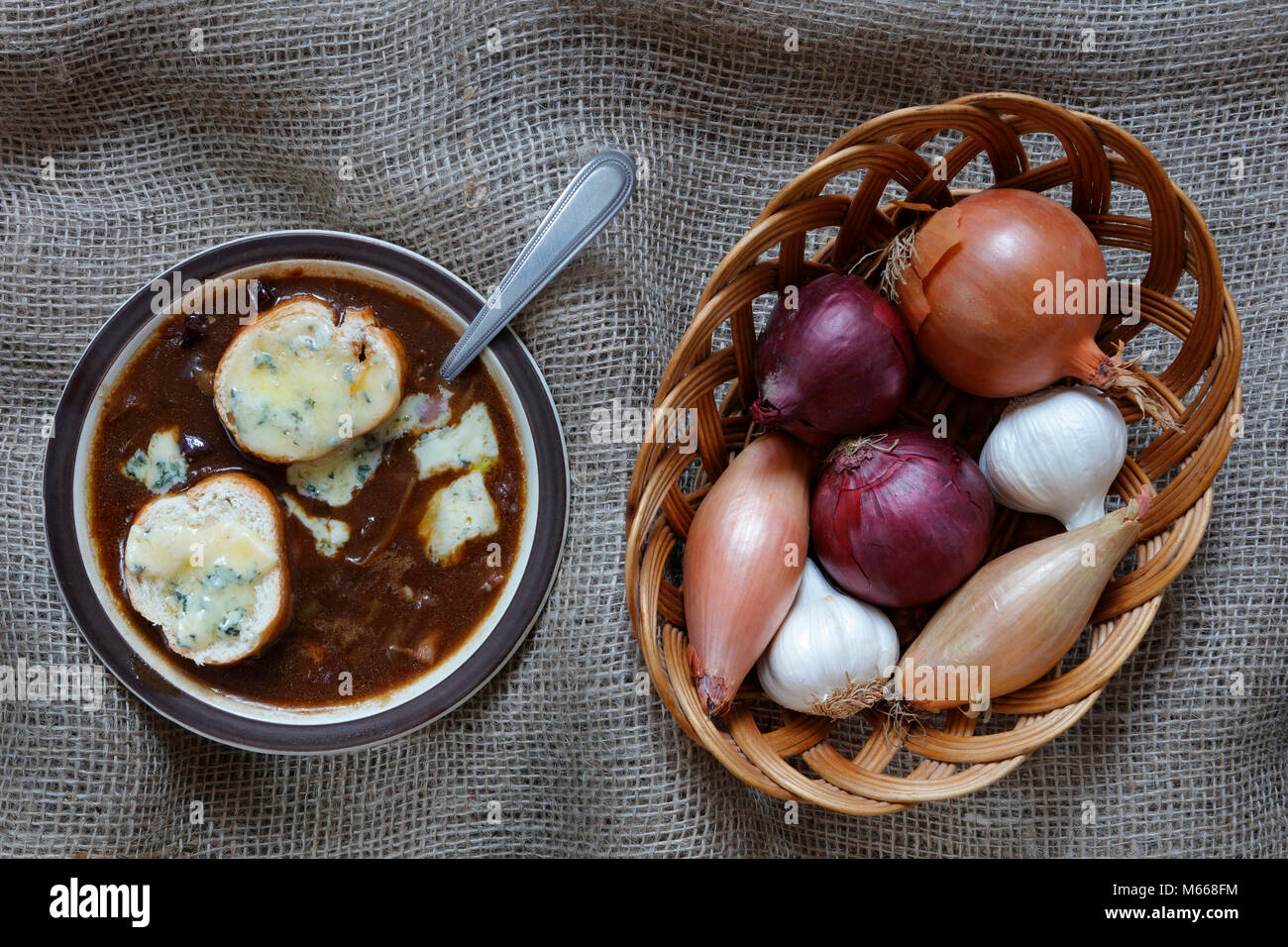 Onion Soup with blue stilton gruyere cheese with Garlic, French Echalion Shallots and red and brown onions in a wicker basket on a hessian cloth backg Stock Photo