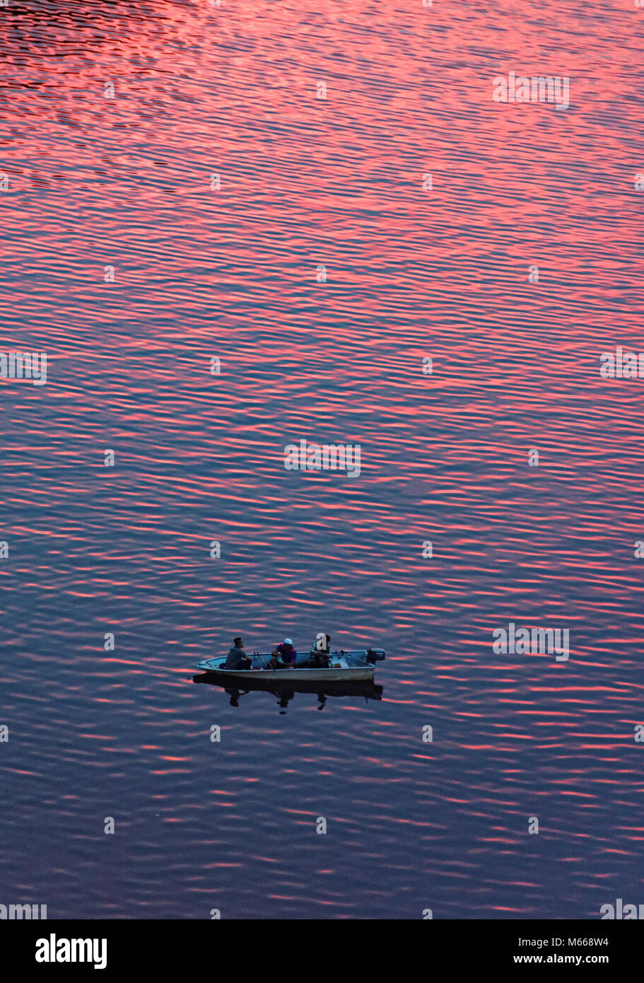 Three men fishing on the Sarawak River in Kuching as the sunset makes the water look red Stock Photo