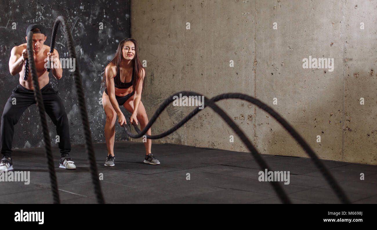 Woman and man couple training together doing battling rope workout ...