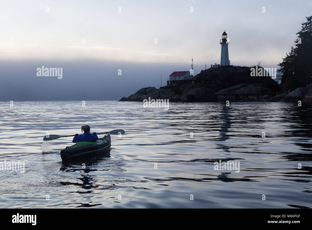 Adventurous woman is sea kayaking near a lighthouse during a vibrant