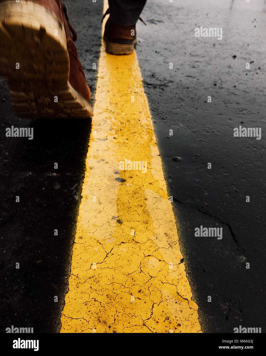 Man walking along a yellow line on the road Stock Photo