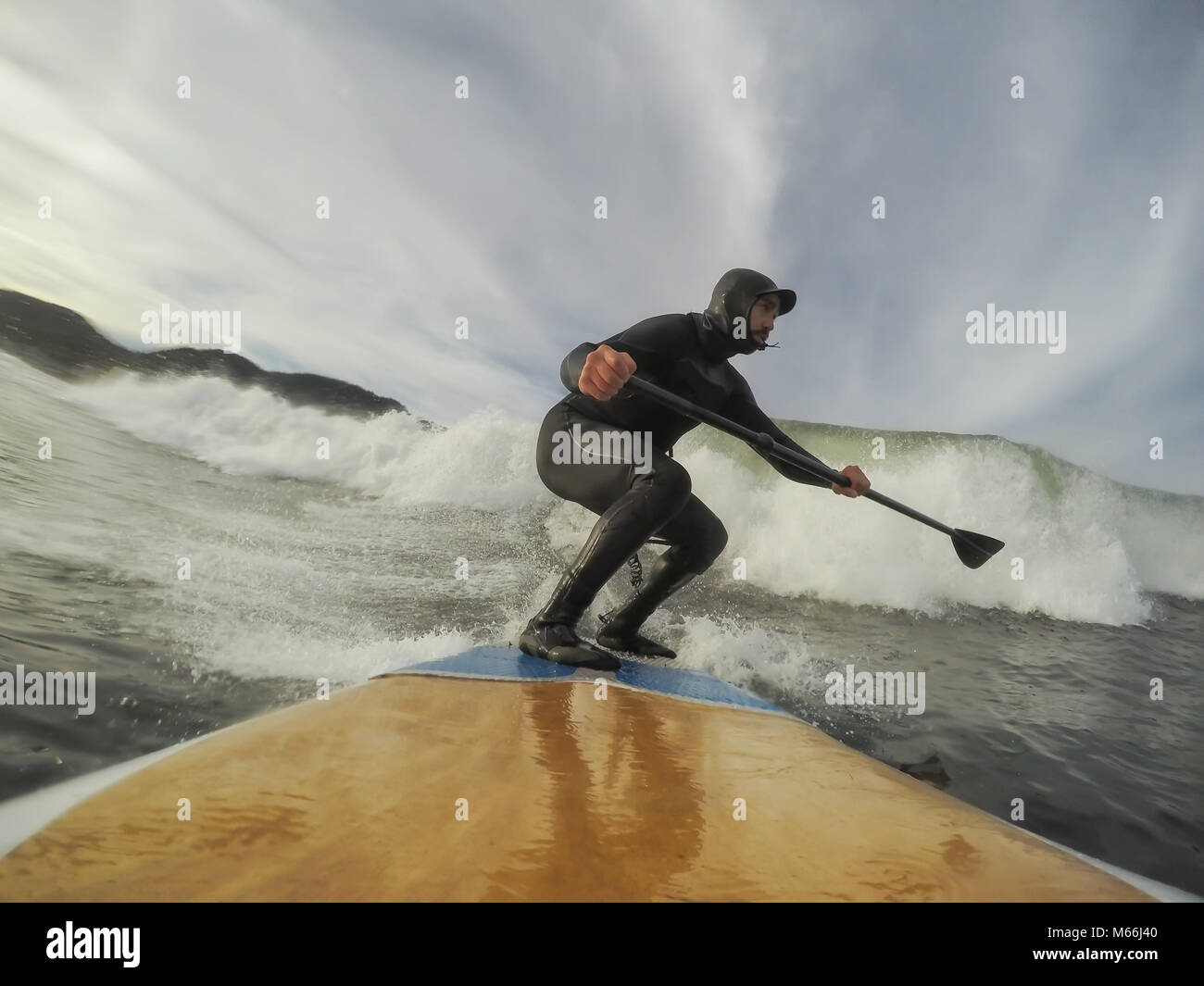 Man in a wetsuit is paddle boarding on a wave in the ocean during a
