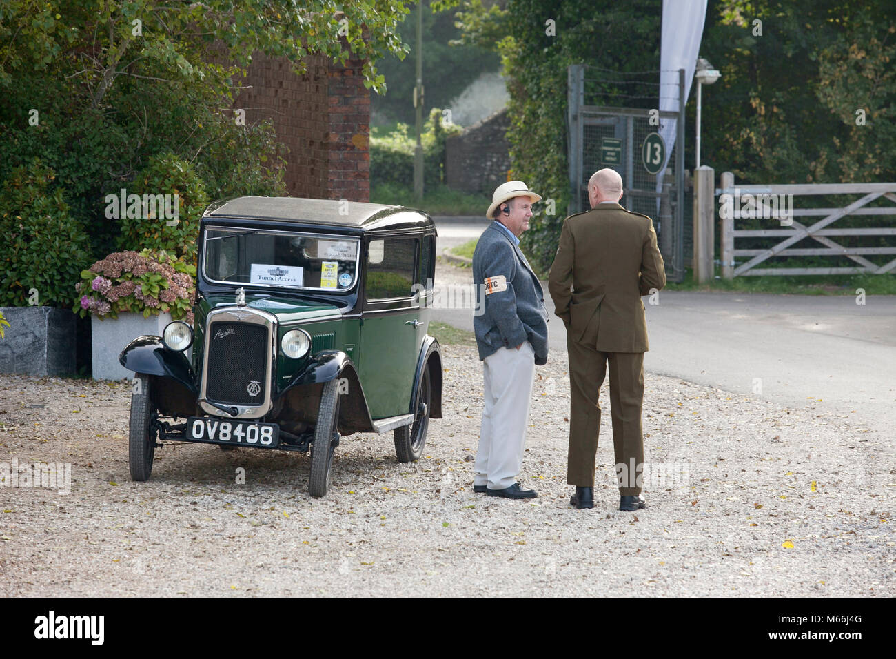 Classic green 1930's Austin car in green with black roof and two men in vintage clothes standing close to the vehicle in the grounds of goodwood Stock Photo