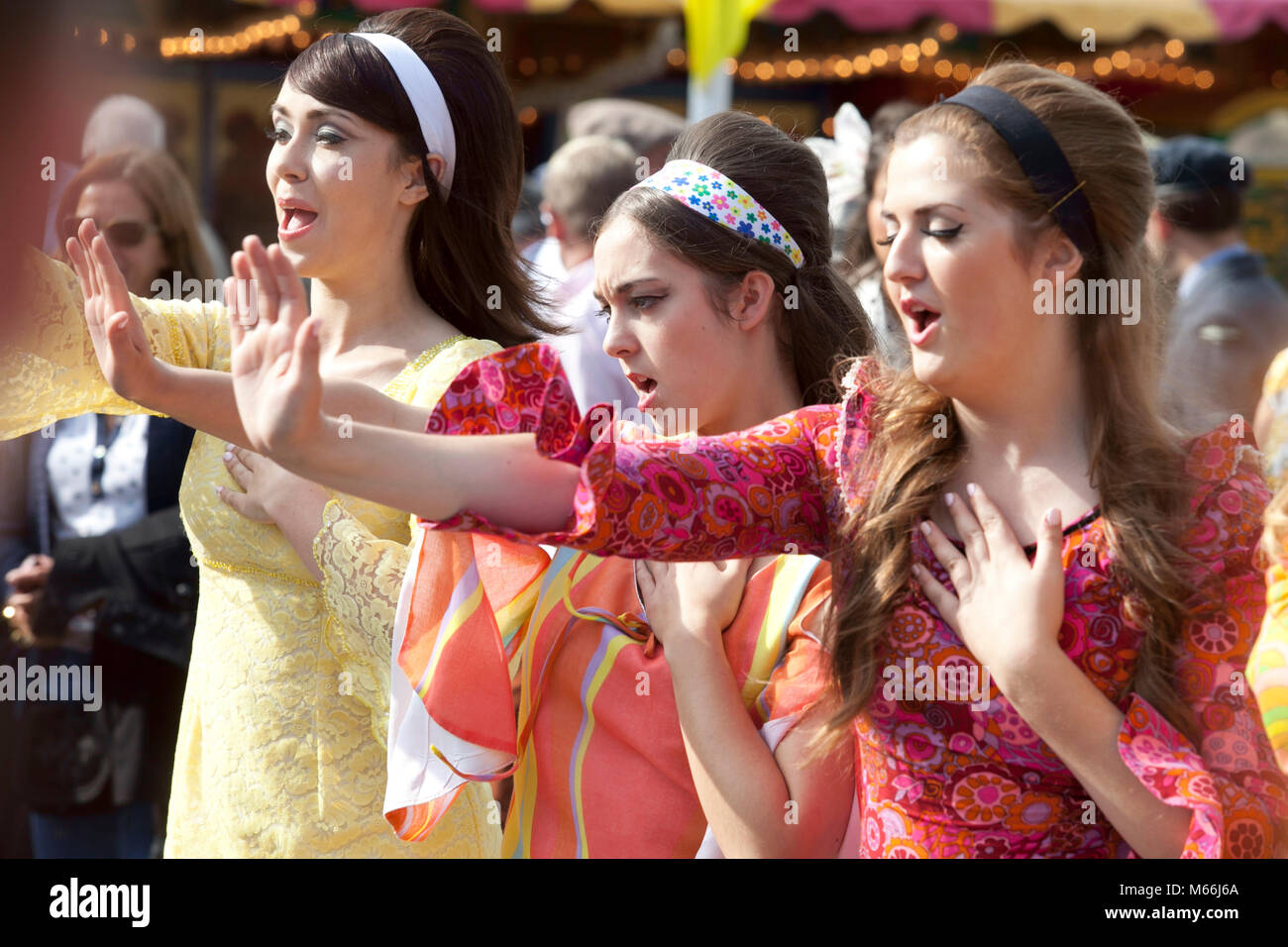 Three young women in brightly coloured 1960's style dresses looking happy attending the Goodwood revival meeting Stock Photo