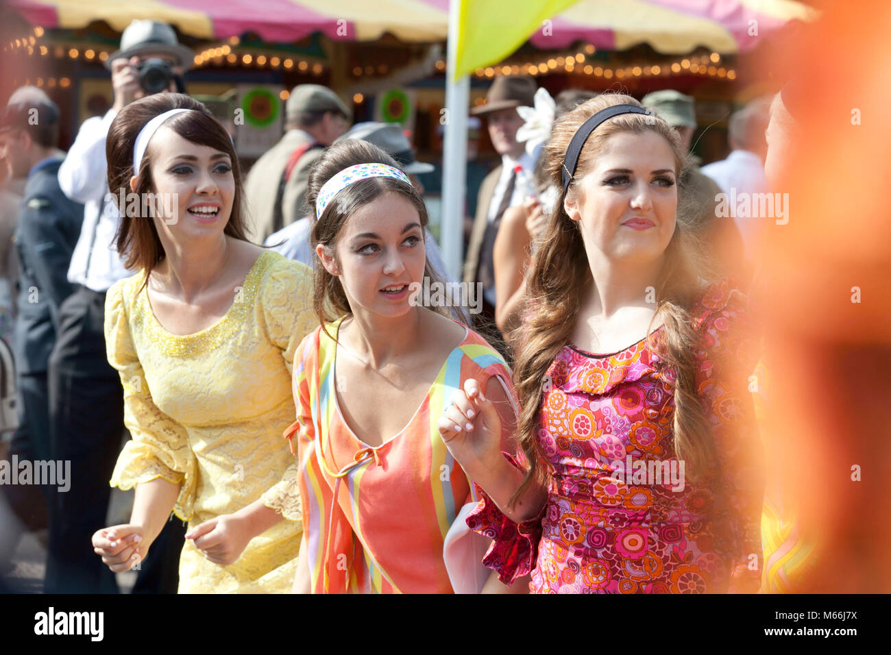 Three young women in brightly coloured 1960's style dresses looking happy attending the Goodwood revival meeting Stock Photo