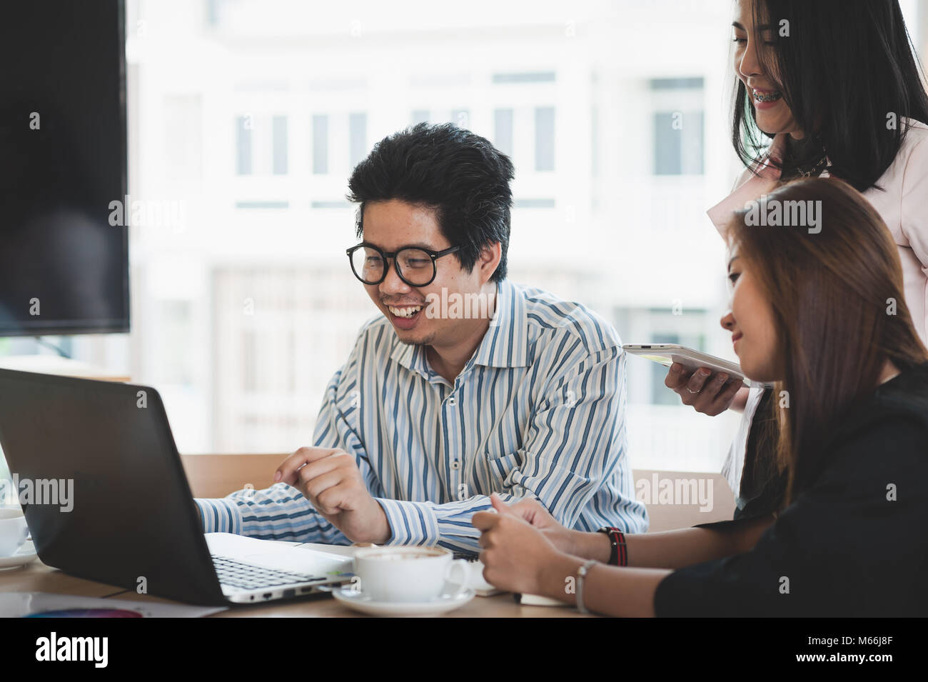 Young Asian businessman and businesswoman talking about their work while looking at laptop monitor in meeting room. Startup business brainstorm concep Stock Photo