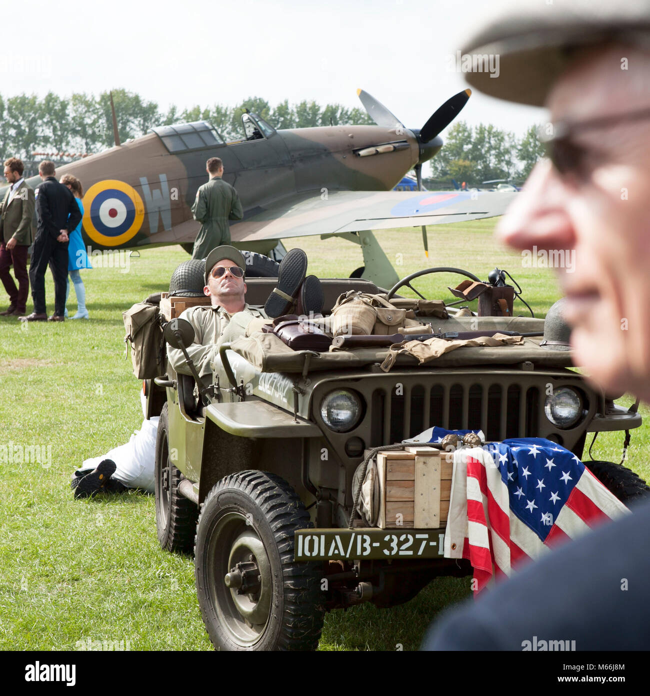 Willis jeep with American flag on airfield with RAF spitfire plane in the background on location at the Goodwood revival event in sussex Stock Photo