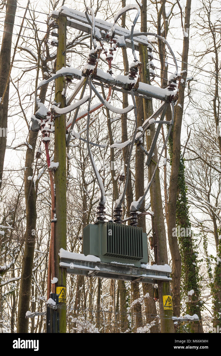 Three phase pole mounted high voltage mains transformer frozen with snow and icicles causing electricity distribution problems on National Grid local Stock Photo