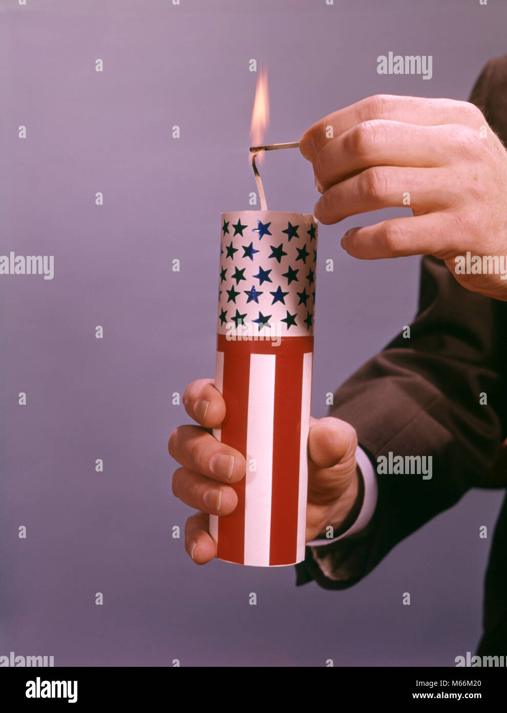 MALE HANDS LIGHTING A GIANT RED WHITE AND BLUE AMERICAN FIRECRACKER - kf5437 HAR001 HARS MATCH DANGER RISK INDOORS STRIPES AMERICANA NOSTALGIA 20-25 YEARS FREEDOM SINGLE OBJECT DANGEROUS AND EXCITEMENT LIT 18-19 YEARS 1776 MATCHES PATRIOT POLITICS FIRECRACKER CONCEPTUAL STILL LIFE CLOSE-UP FIRECRACKERS PATRIOTIC SYMBOLIC EXPLODE MALES RED WHITE AND BLUE YOUNG ADULT MAN CAUCASIAN ETHNICITY FOURTH OF JULY FUZE IGNITING INDEPENDENCE DAY JULY 4TH OLD FASHIONED PERSONS WICK Stock Photo