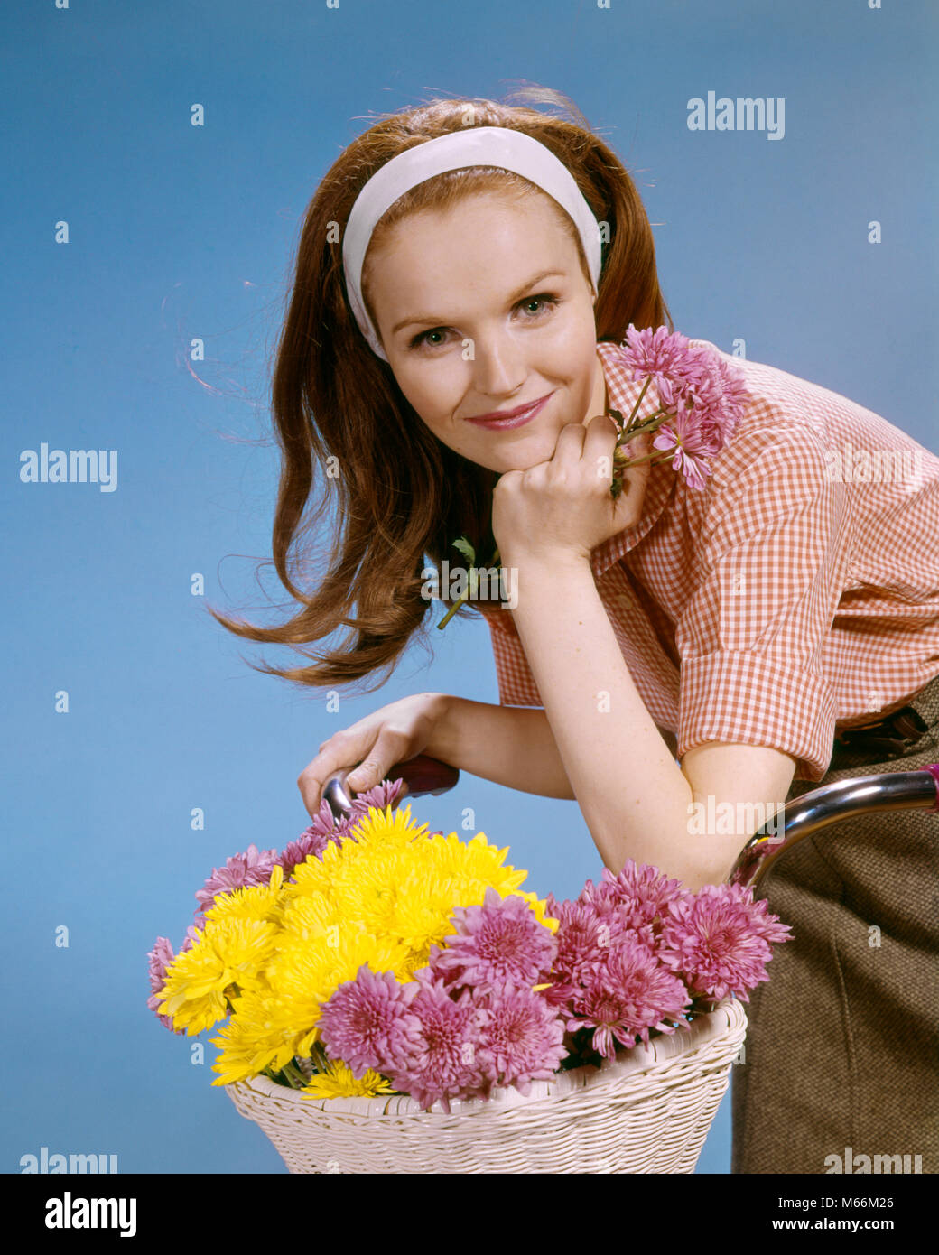 1960s SMILING REDHEAD YOUNG WOMAN RIDING BICYCLE WITH BASKET OF FLOWERS LOOKING AT CAMERA - kf5477 HAR001 HARS FEMALES STUDIO SHOT BIKING GROWNUP HEALTHINESS ONE PERSON ONLY HOME LIFE COMMUNICATING TRANSPORT COPY SPACE HALF-LENGTH LADIES GROWN-UP INDOORS TRANSPORTATION NOSTALGIA EYE CONTACT 20-25 YEARS RIDER YOUNGSTER HAPPINESS LEISURE RECREATION REDHEAD 18-19 YEARS RED HAIR GOOD HEALTH COMMUNICATE MOBILITY YOUNG ADULT WOMAN CAUCASIAN ETHNICITY LOOKING AT CAMERA OLD FASHIONED PERSONS Stock Photo