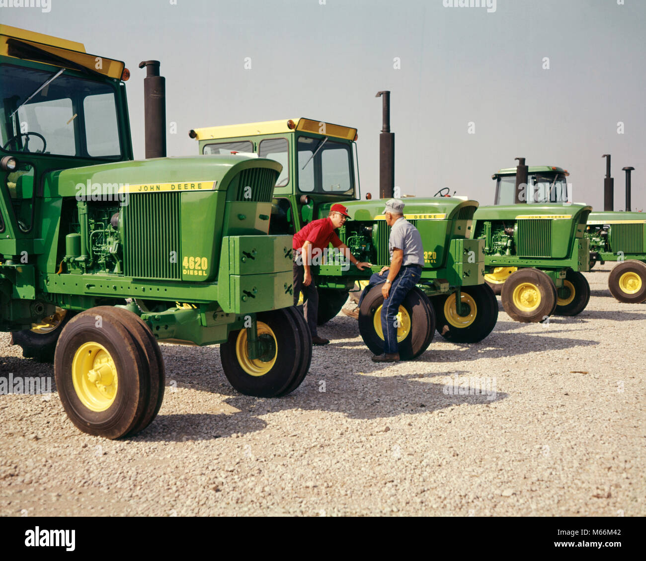 1960s TWO MEN FARMERS INSPECTING DISPLAY OF JOHN DEERE TRACTORS AT FARM