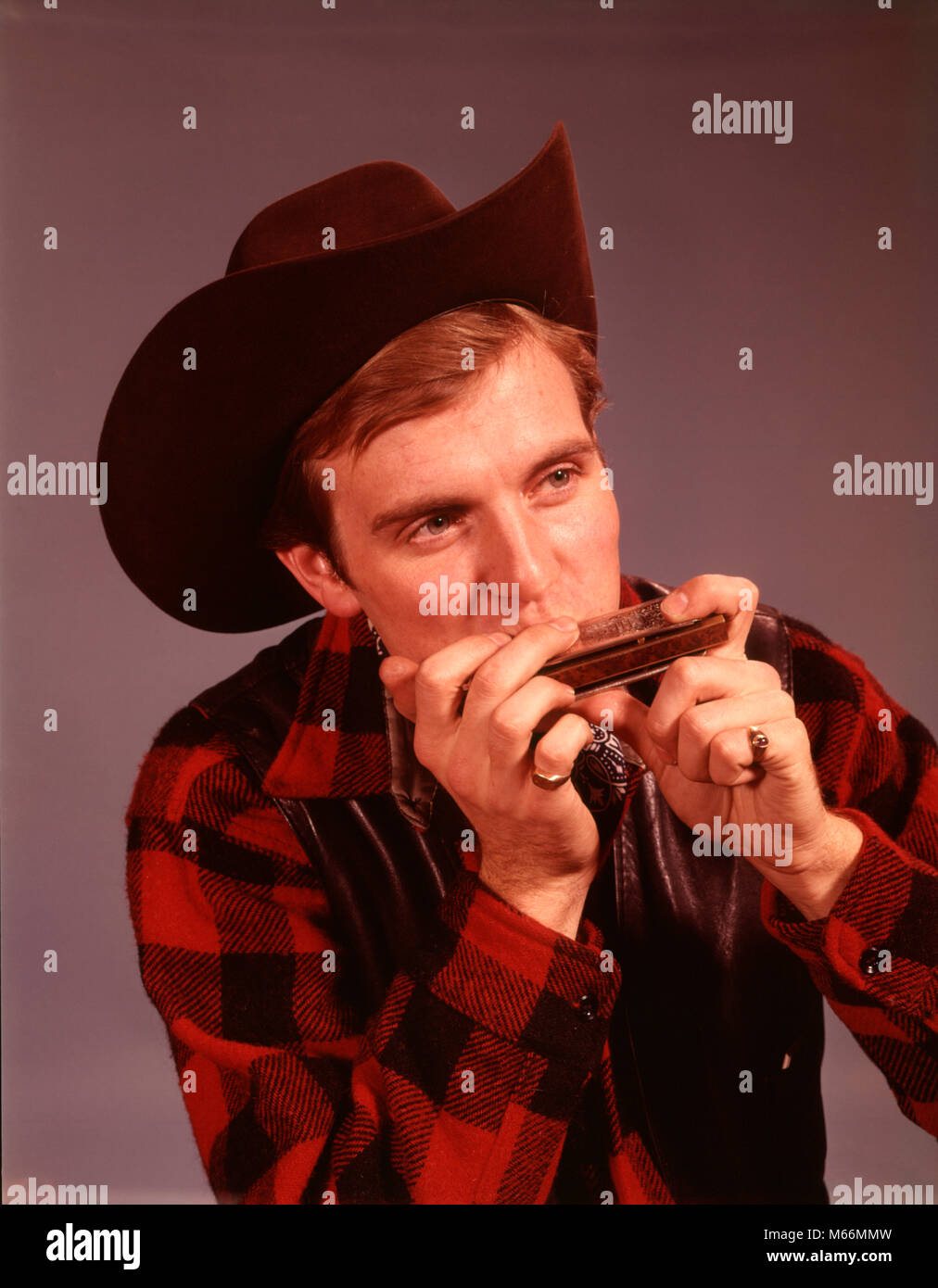 1960s MAN PLAYING HARMONICA WEARING COWBOY HAT COUNTRY WESTERN MUSICIAN  PERFORMER - km1284 HAR001 HARS COMMUNICATING WOOL COPY SPACE HALF-LENGTH  GROWN-UP CHARACTER WESTERN INDOORS PLAID PROFESSION ENTERTAINMENT  CONFIDENCE AMERICANA NOSTALGIA 20-25 YEARS