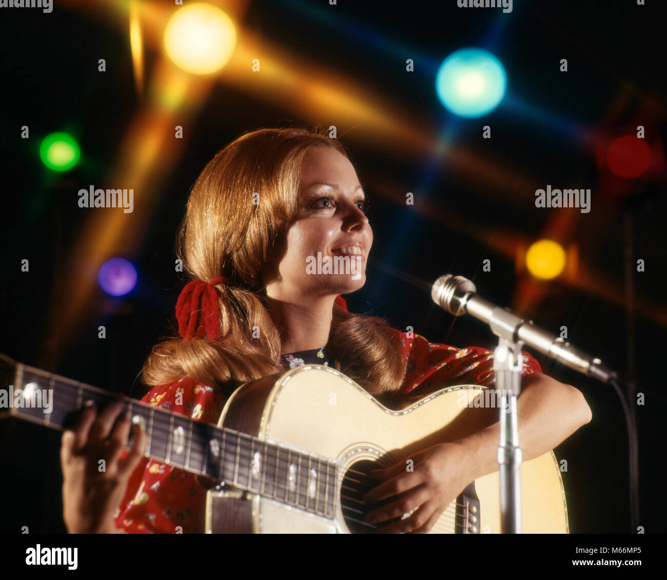 1970s WOMAN FOLK SINGER GUITAR SINGING INTO MICROPHONE COLORFUL SPOTLIGHTS - km3877 HAR001 HARS DREAMS OCCUPATION HAPPINESS HEAD AND SHOULDERS PERFORMER CAREERS SONG VOCAL 18-19 YEARS ENTERTAINER MUSICAL INSTRUMENT VOCALIZE VOCALS FOLK PERFORMERS SONGS ENTERTAINERS SPOTLIGHTS YOUNG ADULT WOMAN CAUCASIAN ETHNICITY FOLK SINGER OCCUPATIONS OLD FASHIONED PERSONS Stock Photo