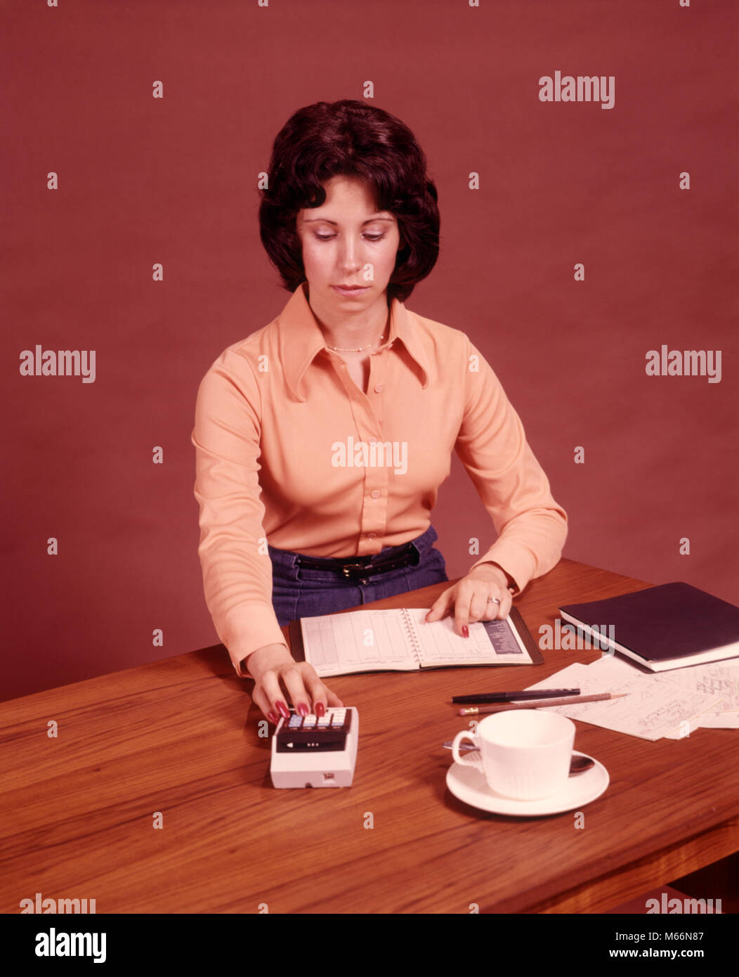 1970s YOUNG WOMAN SITTING AT DESK USING CALCULATOR TO BALANCE BUDGET - ks12329 HAR001 HARS GROWN-UP INDOORS PORTABLE NOSTALGIA 20-25 YEARS 25-30 YEARS HOMEMAKER YOUNGSTER HOMEMAKERS CHECKBOOK LABOR EMPLOYMENT HOUSEWIVES SMALL GROUP OF OBJECTS EMPLOYEE PERSONAL FINANCE ELECTRONIC MID-ADULT MID-ADULT WOMAN PEOPLE ADULTS TAXES CALCULATING CAUCASIAN ETHNICITY LABORING OLD FASHIONED PERSONS SAUCER Stock Photo