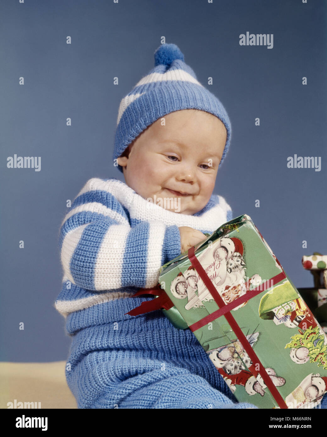 1960s BABY BOY BLUE WHITE KNIT OUTFIT EXCITED OPENING CHRISTMAS PRESENT - kx4916 HAR001 HARS NOSTALGIA KNIT HAPPINESS HEAD AND SHOULDERS EXCITEMENT SMILES DECEMBER JOYFUL DECEMBER 25 BABY BOY 1-6 MONTHS 6-12 MONTHS JUVENILES MALES CAUCASIAN ETHNICITY OLD FASHIONED Stock Photo