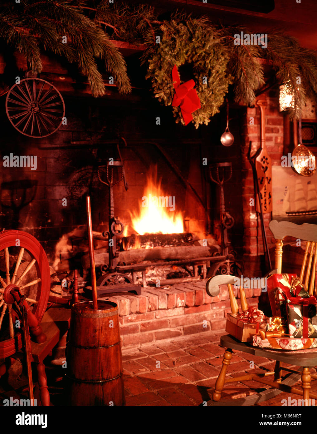 1960s COLONIAL STYLE FIREPLACE FIRE BLAZING DECORATED CHRISTMAS WREATH CHAIR WITH PRESENTS AND GIFTS - kx4923 HAR001 HARS OLD FASHIONED Stock Photo