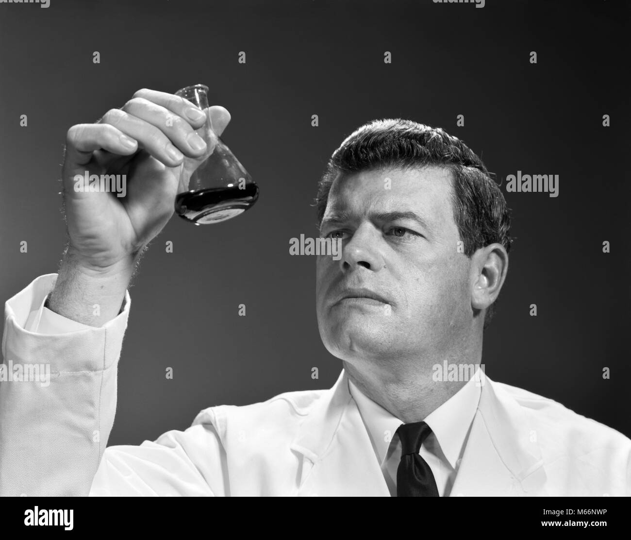 1960s 1970s MAN SCIENTIST HOLDING LOOKING AT GLASS BEAKER OF LIQUID - l2492 HAR001 HARS OCCUPATION HEAD AND SHOULDERS CHEMICAL DISCOVERY CHEMIST SCIENTIFIC BEAKER KNOWLEDGE PHARMACEUTICAL PROGRESS INNOVATION HIGH TECH RESEARCHING SOLUTIONS FLASK MALES MID-ADULT MID-ADULT MAN TEST TUBE B&W BLACK AND WHITE CAUCASIAN ETHNICITY OCCUPATIONS OLD FASHIONED PERSONS Stock Photo