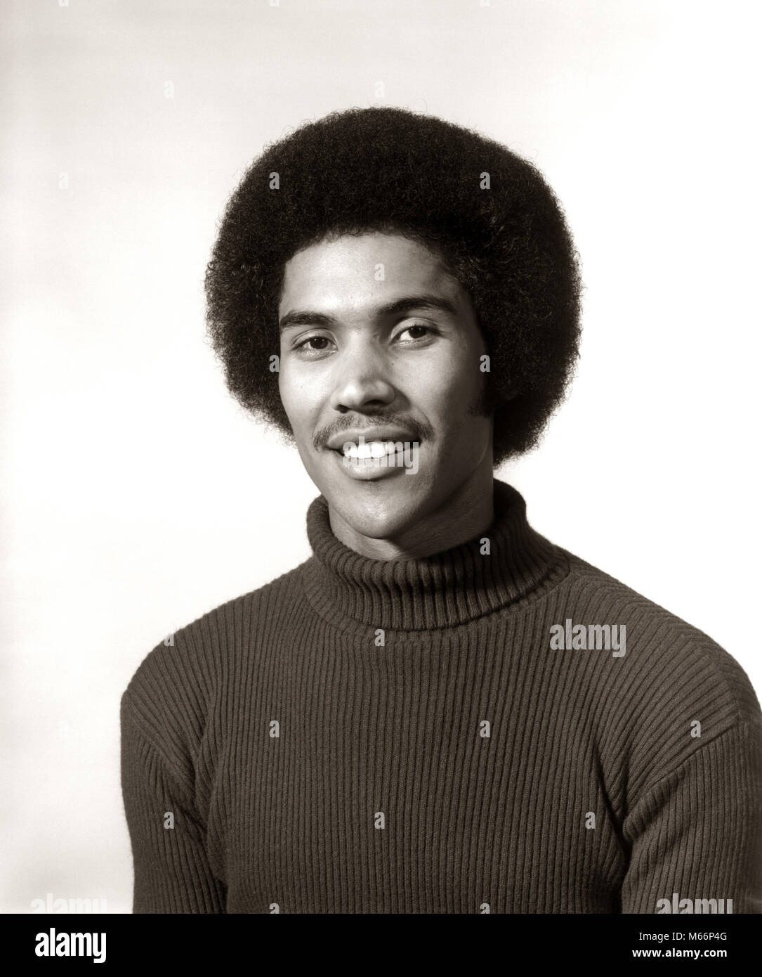1970s 1975 SMILING AFRICAN AMERICAN MAN PORTRAIT WEARING TURTLENECK SWEATER AFRO HAIR STYLE LOOKING AT CAMERA - p8235 HAR001 HARS AFRICAN AMERICANS PRIDE AFRICAN AMERICAN R SMILES JOYFUL PANORAMIC HAIRDO MALES PEOPLE ADULTS YOUNG ADULT MAN AFRO HAIR STYLE B&W BLACK AND WHITE LOOKING AT CAMERA OLD FASHIONED PERSONS TURTLENECK Stock Photo