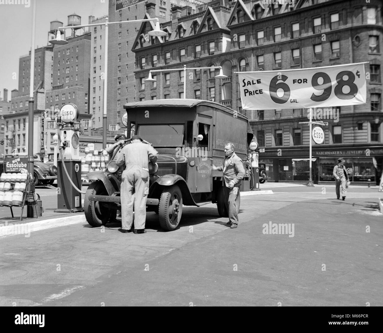 1930s TRUCK FILLING UP AT ESSO GAS STATION ADVERTISING 6 GALLONS FOR 98 CENTS AT BROADWAY & 68th STREET NEW YORK CITY USA - q73971 CPC001 HARS CITIES PRICES VEHICLES NEW YORK CITY SMALL GROUP OF PEOPLE BROADWAY GALLONS PETROLEUM 6 GALLON 68TH 98 98¢ B&W BIG APPLE BLACK AND WHITE CENTS FOSSIL FUEL OCCUPATIONS OLD FASHIONED UPPER WEST SIDE Stock Photo