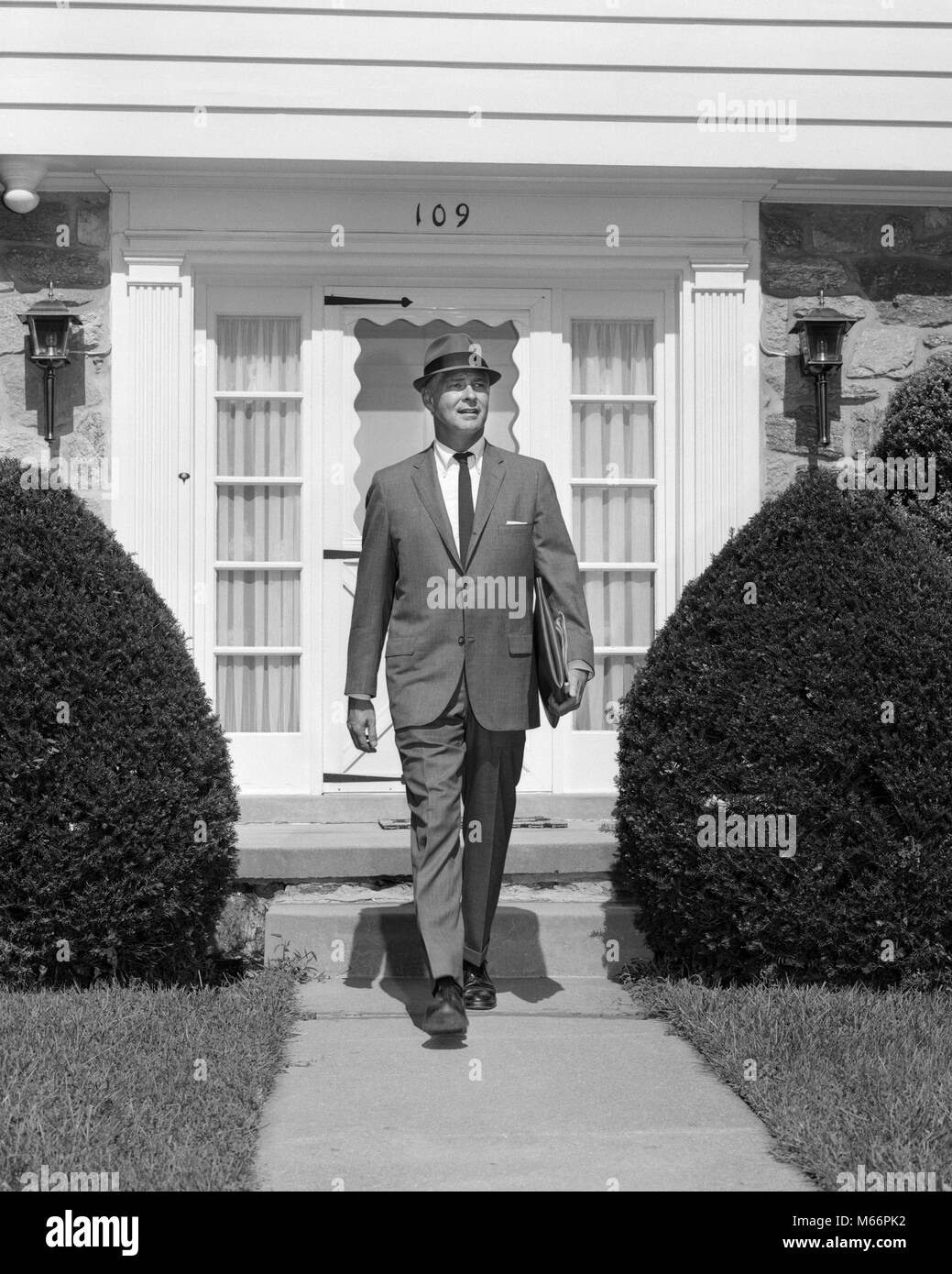 1950s BUSINESSMAN LEAVING SUBURBAN HOUSE HOLDING BRIEFCASE WALKING DOWN SIDEWALK - s15579 HAR001 HARS CAUCASIAN PLEASED LIFESTYLE SALESPERSON GROWNUP HEALTHINESS ONE PERSON ONLY HOME LIFE COPY SPACE FULL-LENGTH GROWN-UP PROFESSION CONFIDENCE NOSTALGIA MORNING 35-40 YEARS 40-45 YEARS WHITE COLLAR OCCUPATION HAPPINESS STYLES PRIDE SMILES FASHIONS SALESMEN MALES MID-ADULT MID-ADULT MAN B&W BLACK AND WHITE CAUCASIAN ETHNICITY DOOR TO DOOR GOING TO WORK OCCUPATIONS OLD FASHIONED PERSONS PORTFOLIO TOWARDS CAMERA Stock Photo
