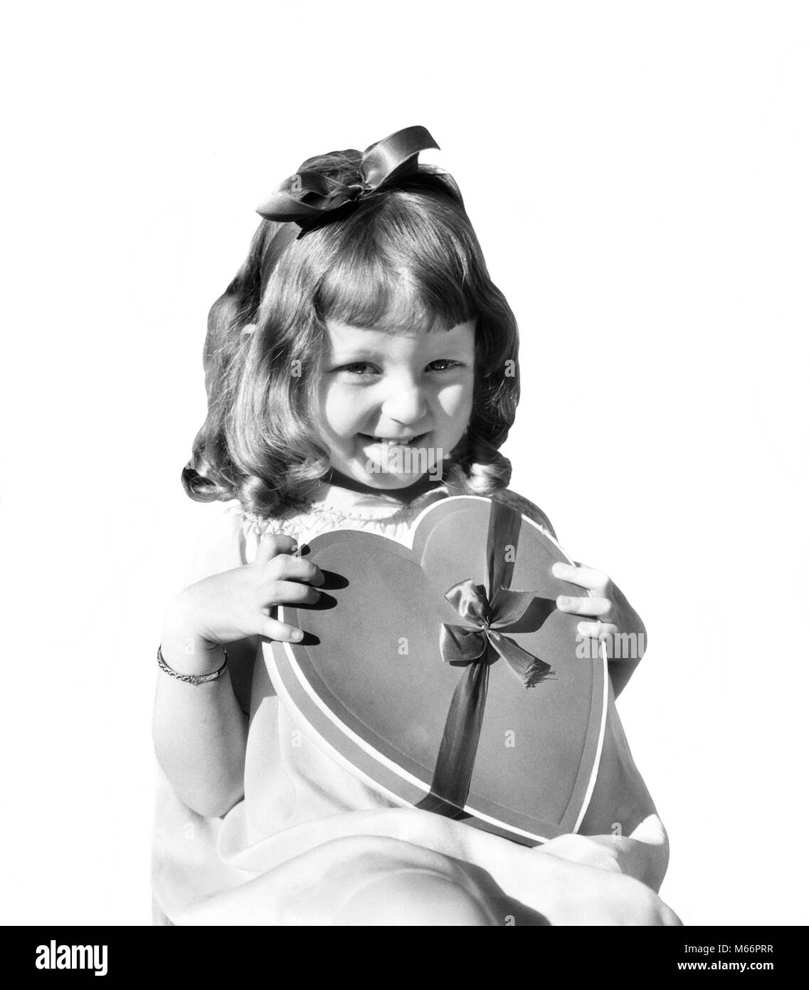 1930s SMILING GIRL JUVENILE HOLDING HEART SHAPED CANDY BOX LOOKING AT CAMERA - v157 HAR001 HARS FRIENDSHIP HALF-LENGTH VALENTINES INDOORS SHAPE SAINT NOSTALGIA EYE CONTACT 7-9 YEARS 5-6 YEARS HAPPINESS CHEERFUL EXCITEMENT VALENTINE'S SMILES JOYFUL ST. SYMBOLIC JUVENILES VALENTINES DAY B&W BLACK AND WHITE CANDIES CAUCASIAN ETHNICITY FEAST DAY FEBRUARY 14 HEART-SHAPED LOOKING AT CAMERA OLD FASHIONED ST. VALENTINE Stock Photo