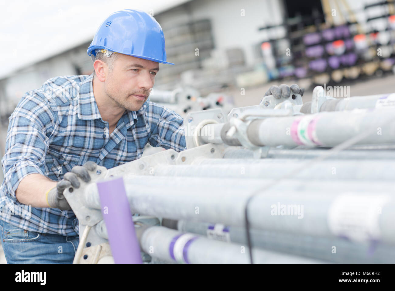 Worker pushing stack of scaffold poles Stock Photo - Alamy