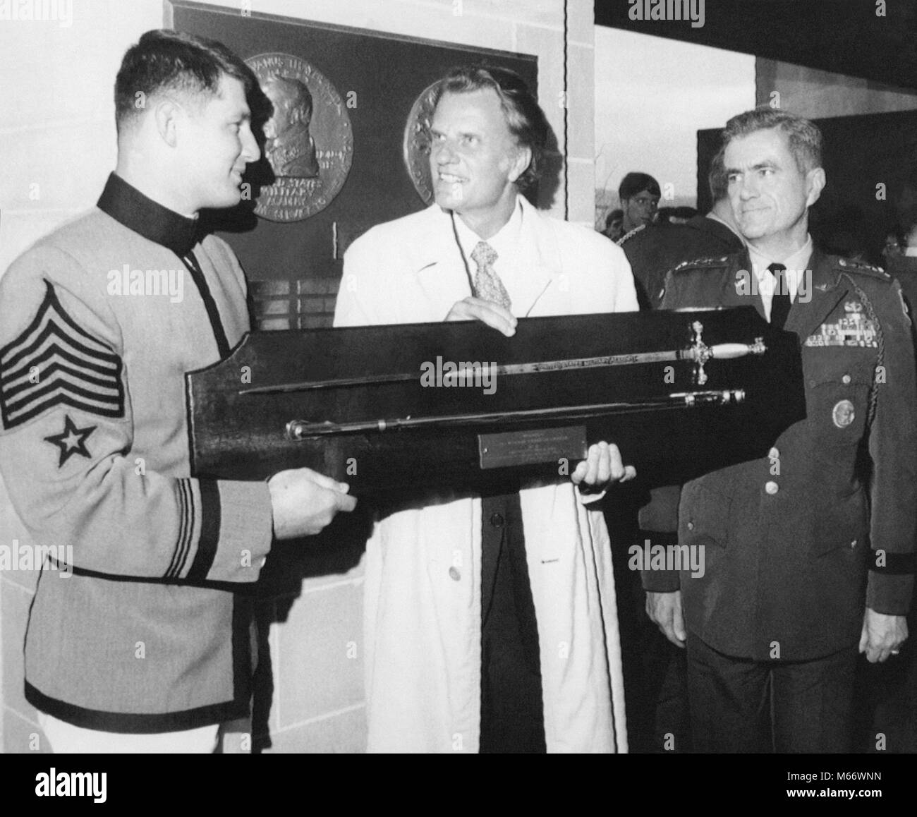 Evangelist Billy Graham (center) receives a ceremonial sword from Cadet Robert Van Antwerp (left) during ceremonies May 4, 1972 at the U.S. Military Academy at West Point, New York where Graham received the Sylvanus Thayer Award for outstanding service to the nation. At right is Lt. Gen. William A. Knowlton, superintendent of the Academy. Stock Photo