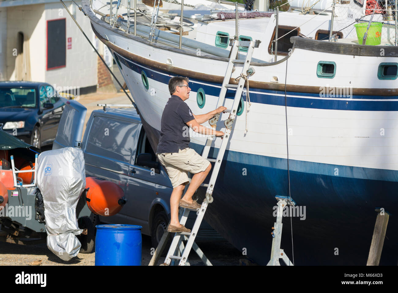 Man climbing up a ladder onto a boat on stands in dry dock, out of