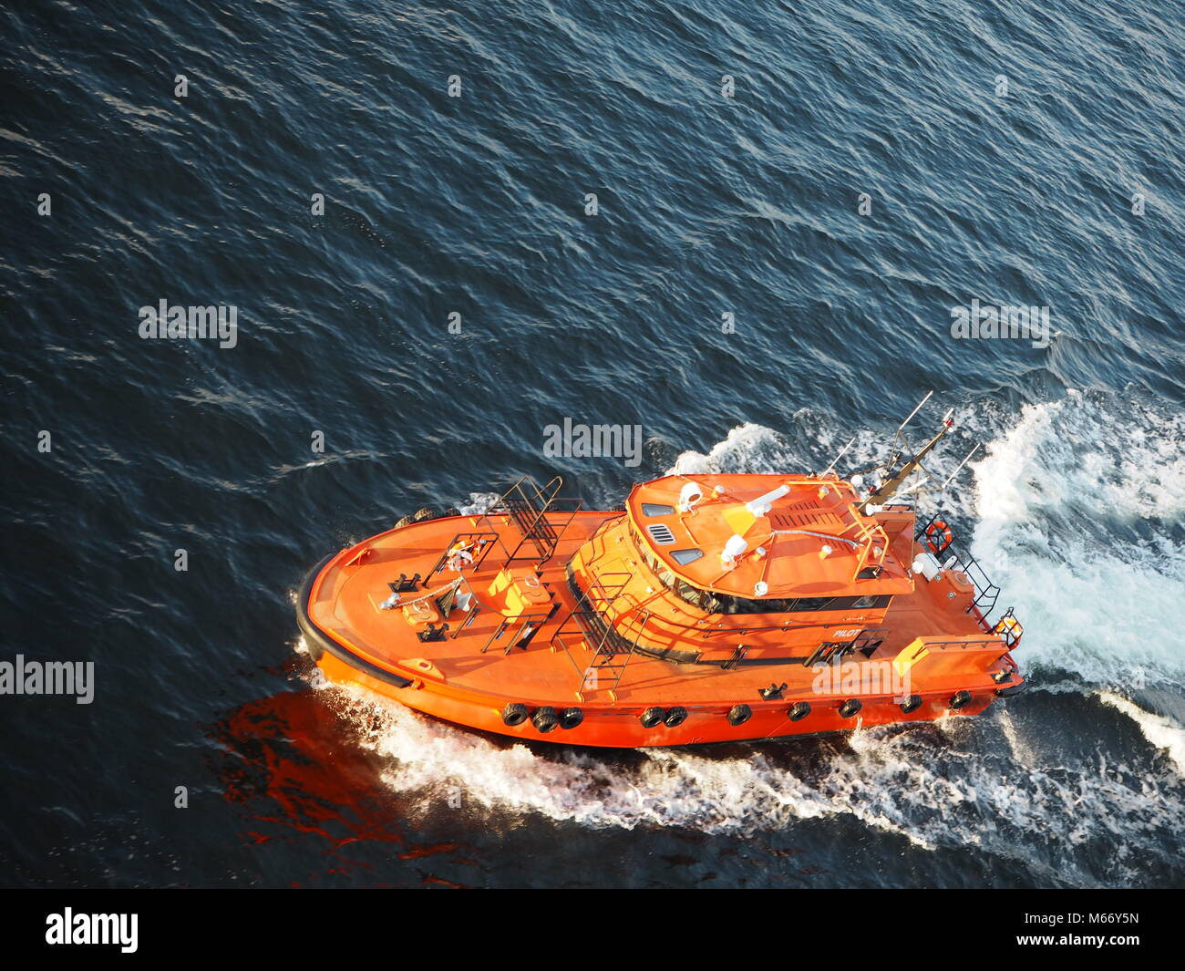 Colorful safety boat leading the huge cruise ship put of the harbor in Stockholm, Sweden. Bright orange boat speeding in the wide, blue ocean. Stock Photo