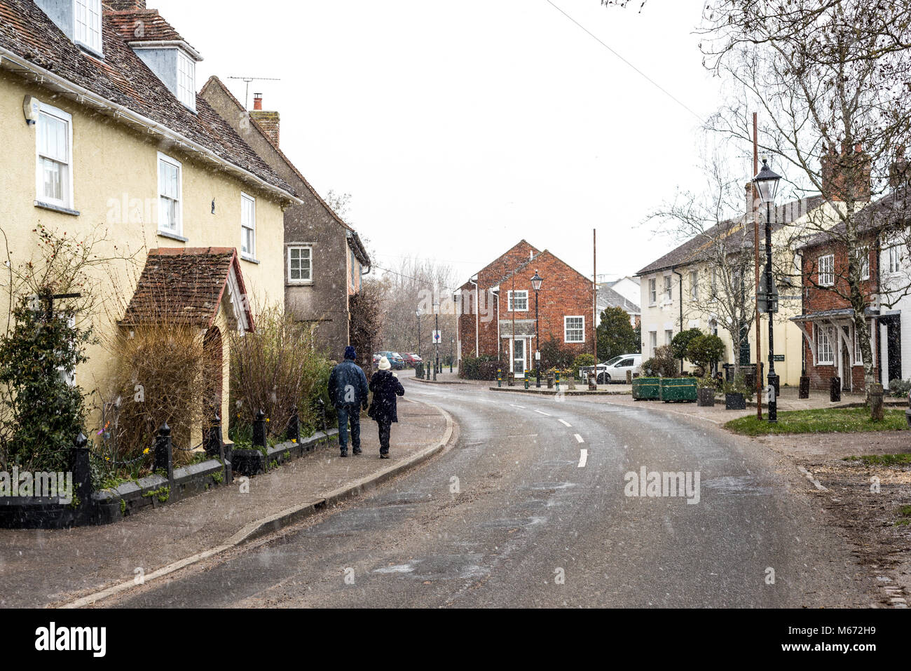 A couple walking down Church Street, Fordingbridge, New Forest, Hampshire, UK, in winter with light snow falling. Stock Photo