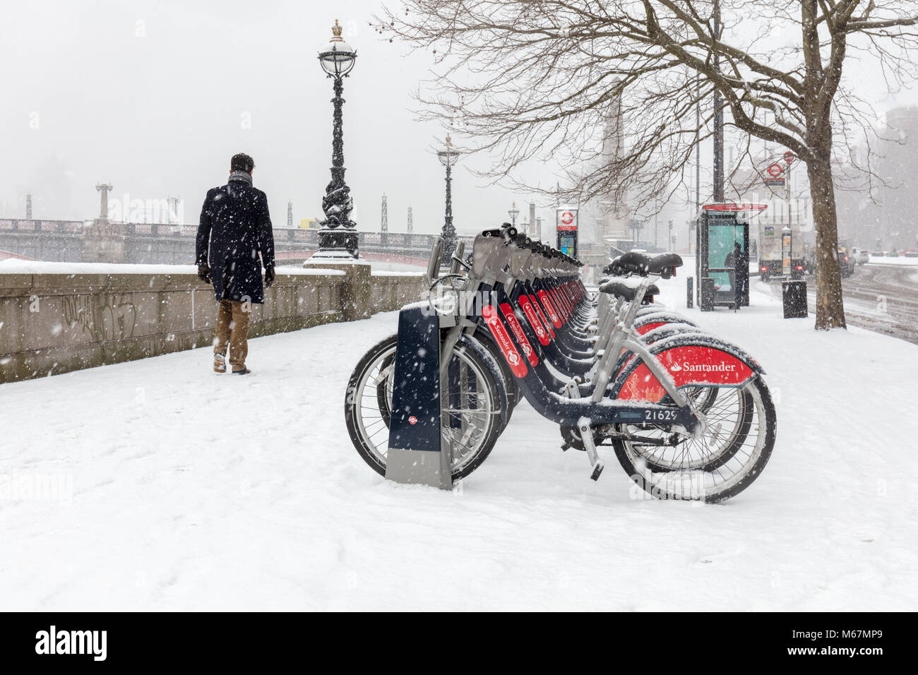 London, UK; 28th February 2018; Man walks past Line of Santander Bikes During Snowstorm Stock Photo