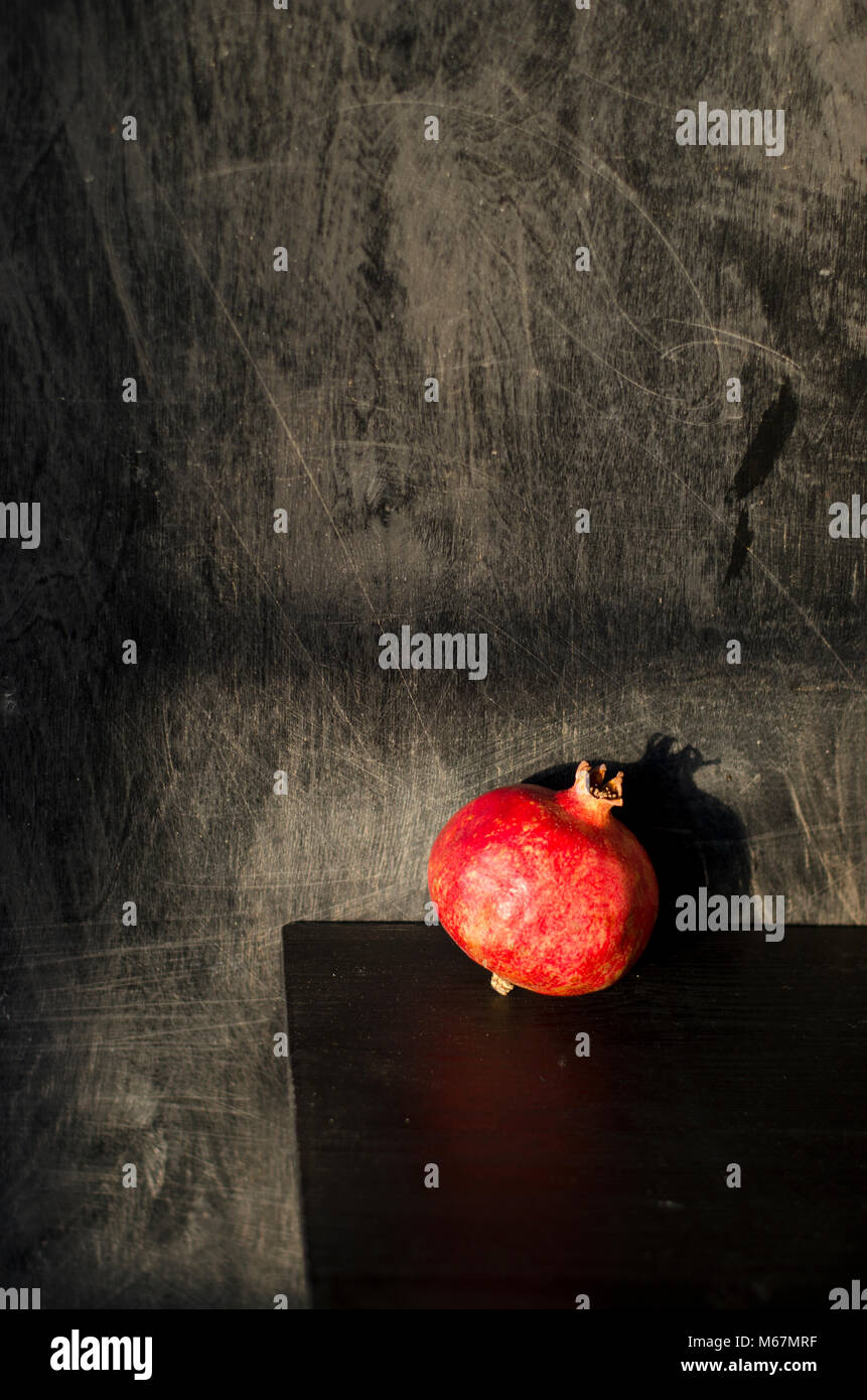 Still-life nature morte with red pomegranate on black wooden background Stock Photo