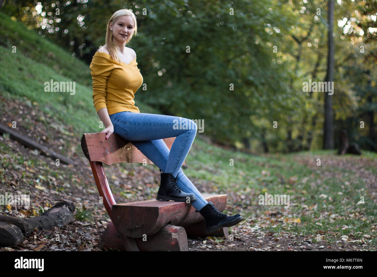 Young beautiful blonde woman sitting on a wooden bench in the park ...