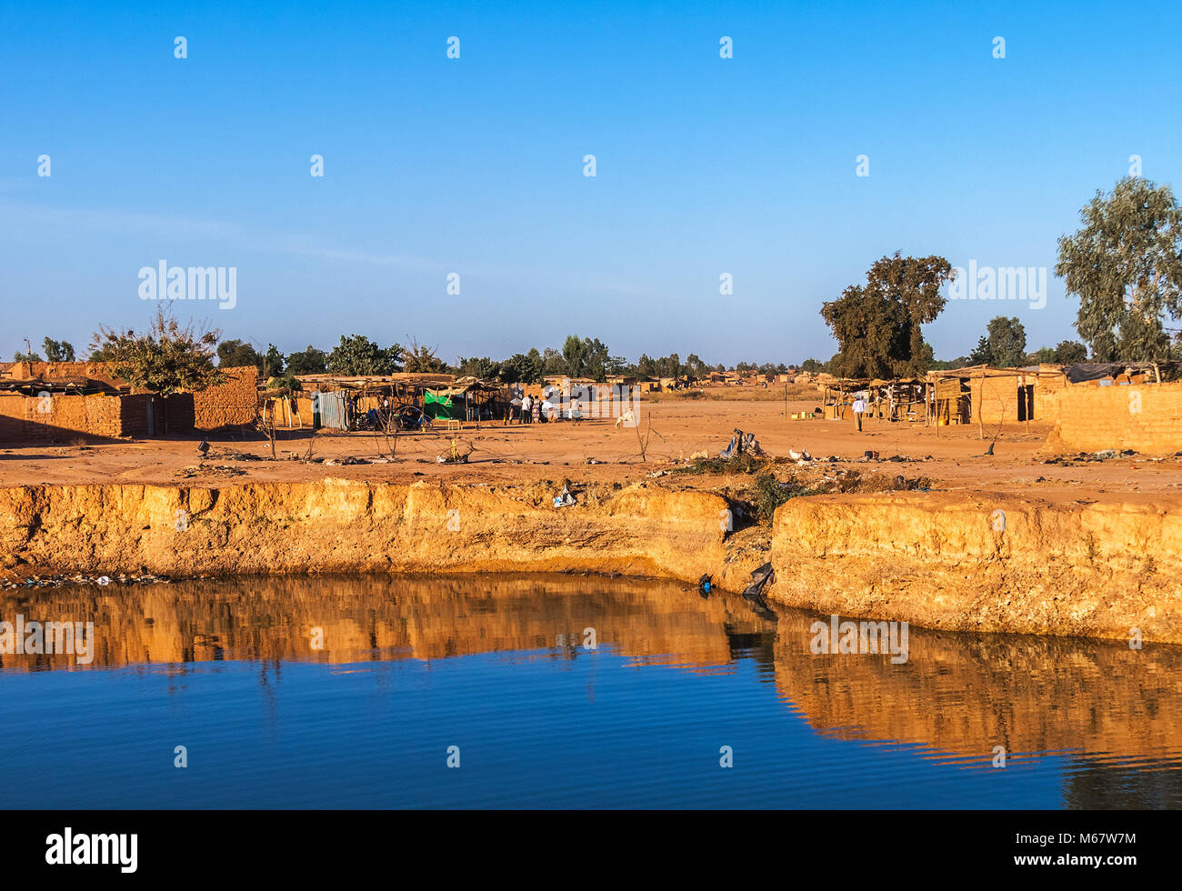 Eastern township of Ouagadougou on a sunny day with a hole filled with rainwater in the foreground, Burkina Faso. Stock Photo