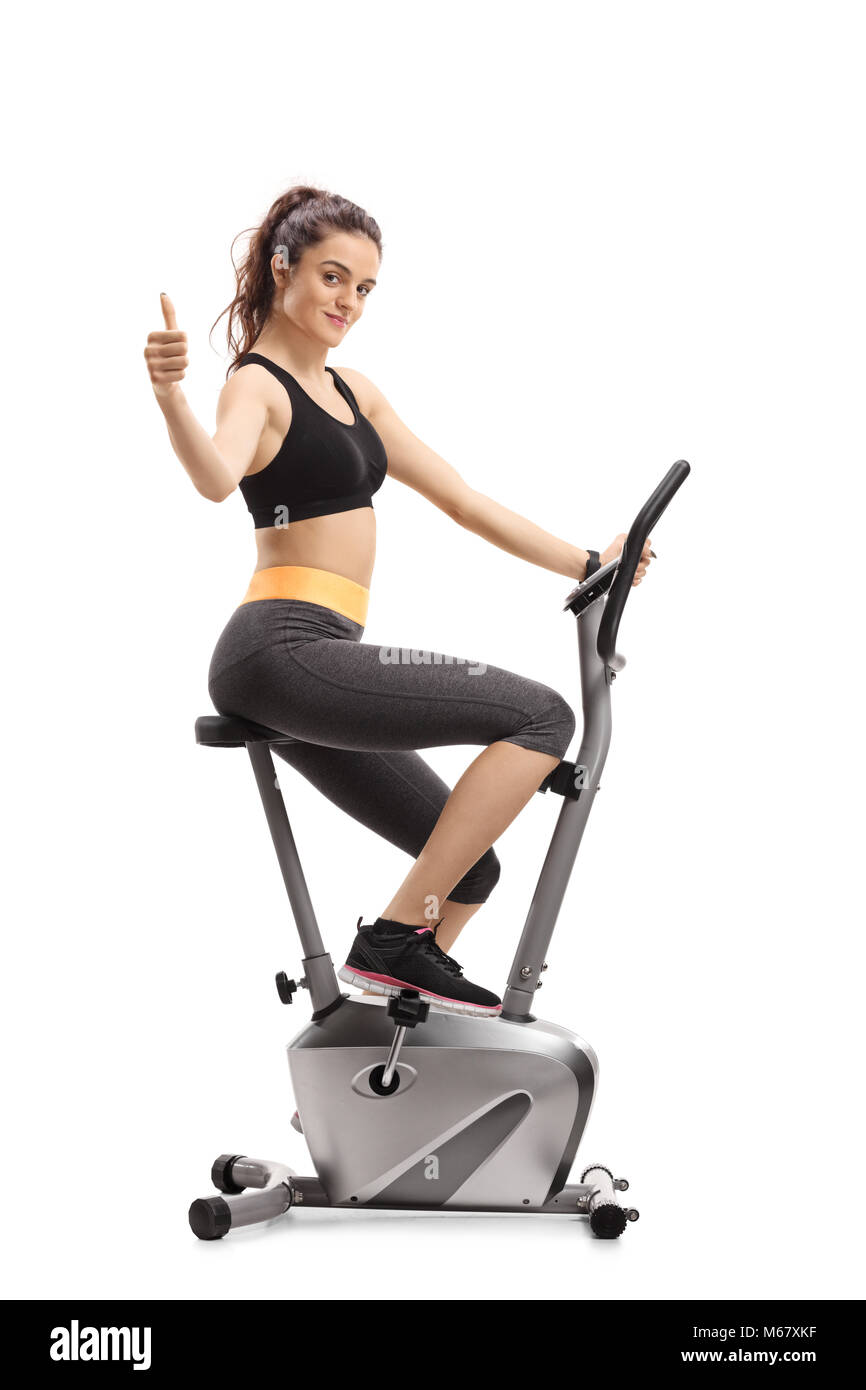 Fitness woman riding an exercise bike and making a thumb up sign isolated on white background Stock Photo
