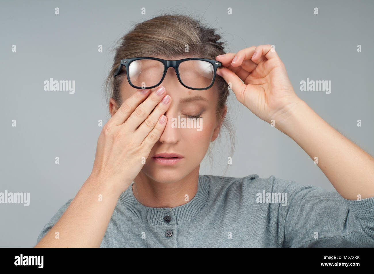 Tired woman in eyeglasses with eyes pain, covering eyes with hands
