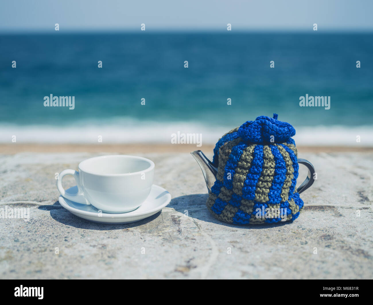 A pot of tea and a cup outside in the sun by the sea Stock Photo