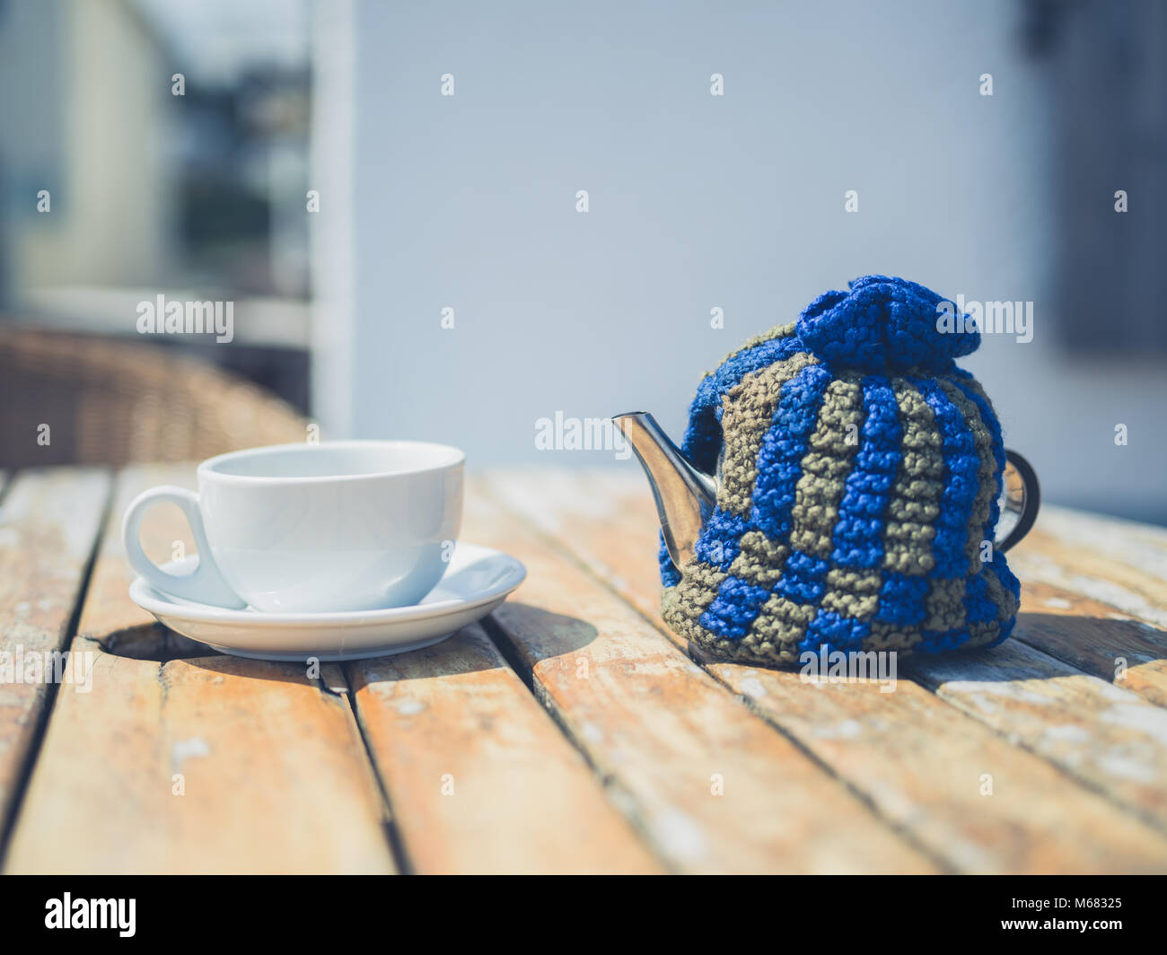 A pot of tea and a cup on a table outside in the sun Stock Photo