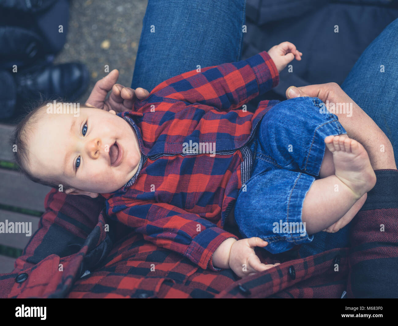 A young father is sitting outside with his baby son in his lap wearing a matching outfit Stock Photo