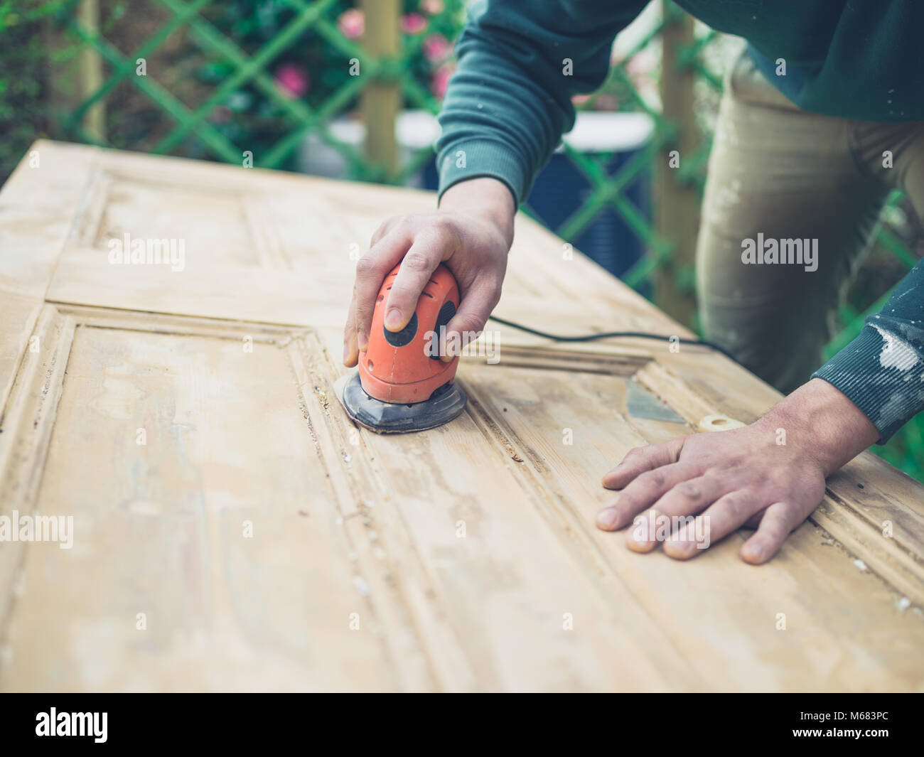 A young man is sanding an old door with an electric sander Stock Photo