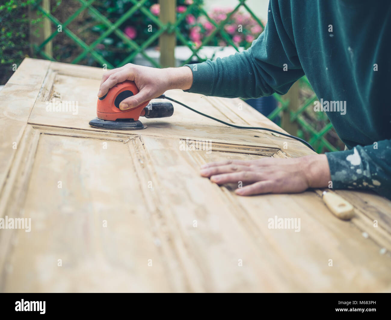 A young man is sanding an old door with an electric sander Stock Photo