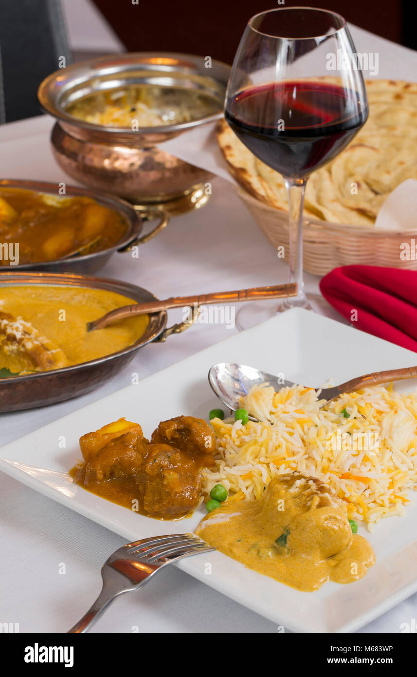 Indian curry food spread on a fancy dinner table with rice, laccha paratha, lamb aam wala, saffron malai kofta, red wine. Stock Photo