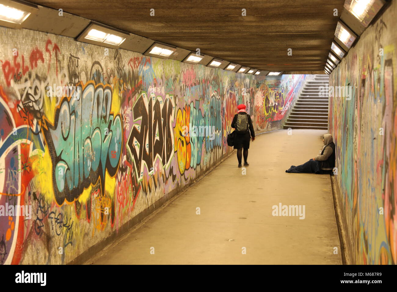 Homeless man begging for money in a subway tunnel covered in graffiti Stock Photo