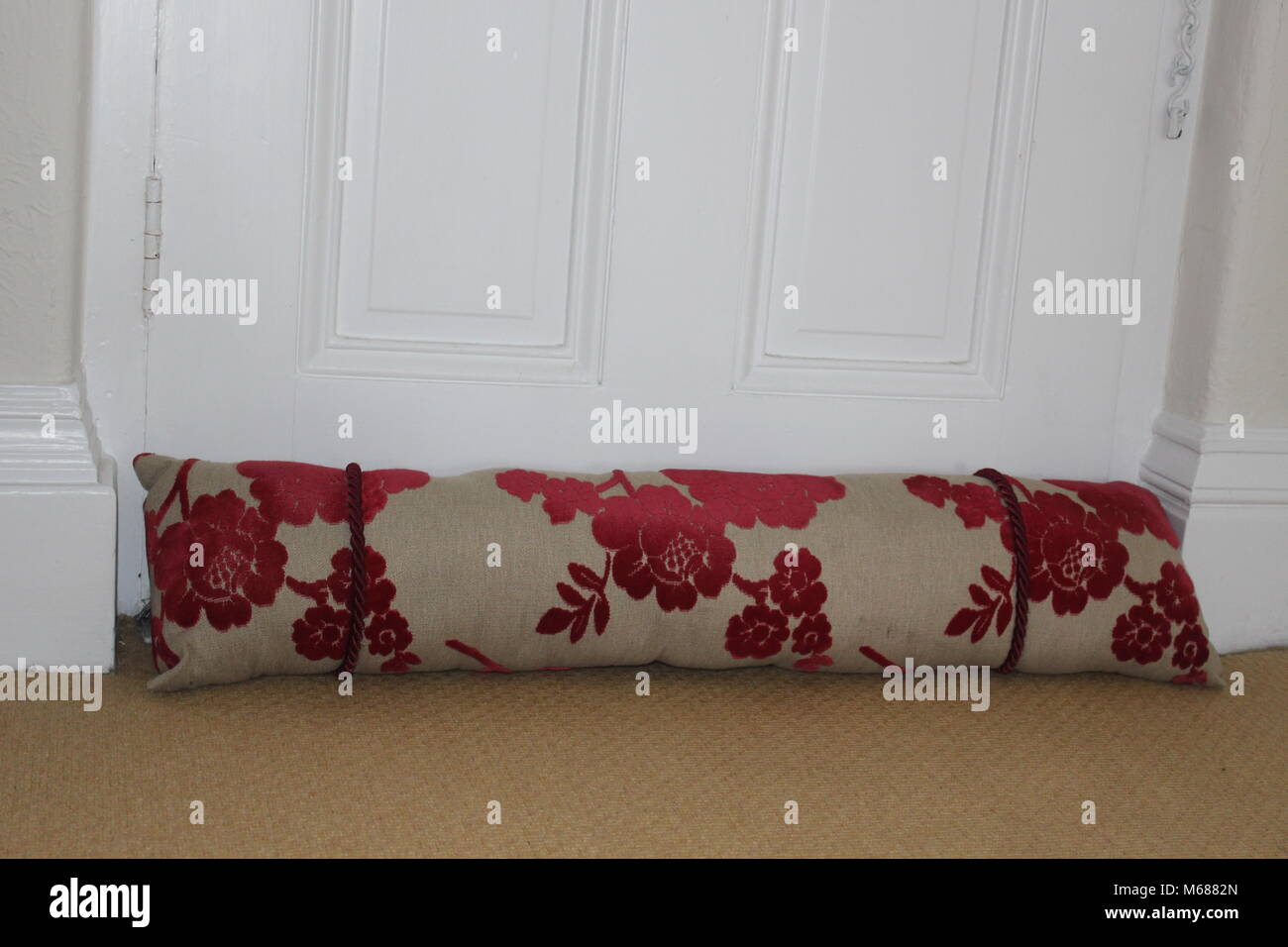 Red and cream draught excluder at the bottom of a white front door in
